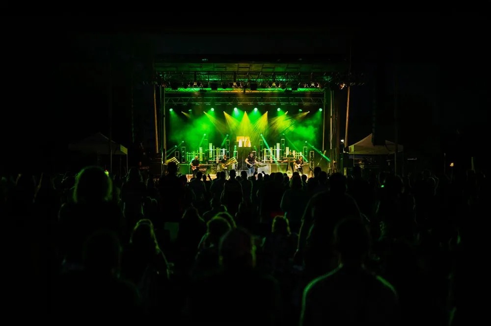 Crowd of people watching a live band perform on stage at a nighttime outdoor concert with green stage lighting.