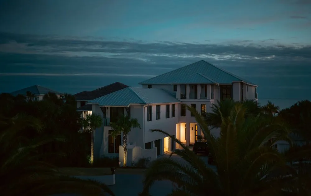 Luxury house with illuminated windows at twilight surrounded by palm trees.