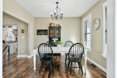 Cozy dining room featuring a white table with black chairs, a chandelier above, and decorative elements like a 'Welcome' sign, all in a neutral-toned space with hardwood floors.