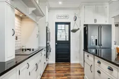 Modern kitchen interior with black countertops, white cabinetry, and a black door labeled "PANTRY".