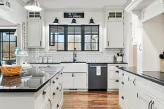 Bright modern farmhouse kitchen with white cabinetry, subway tiles, black countertops, and stainless steel appliances.