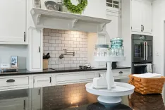 Modern kitchen interior with white cabinetry, subway tile backsplash, black countertops, and stainless steel appliances, accented by decorative greenery and kitchenware on the counters.