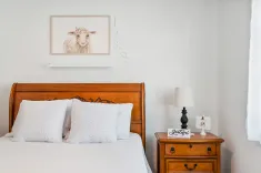 Cozy bedroom details with a wooden bed frame, white textured pillows, a lamp on a wooden bedside table, and wall art featuring a whimsical sheep above the bed.