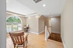 Bright, spacious room with wooden floors, a large arched window, a wooden rocking chair, and stairs leading down.