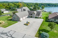 Aerial view of a large residential property with expansive paved driveway, manicured lawn, adjacent to a lake.