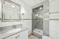 Modern bathroom interior with white and gray design, featuring a walk-in shower, granite countertop with sink, and large mirror.