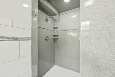 Modern shower interior with gray tiles, built-in shelf, and glass door.