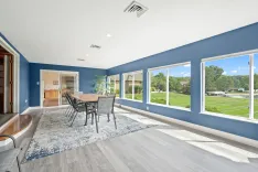 Bright and spacious dining room with blue walls, large windows offering a view of a green lawn, and a wooden table with chairs.