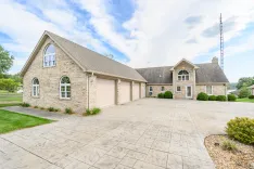 A spacious single-family home with a stone facade, large driveway, and a well-manicured lawn under a partly cloudy sky.
