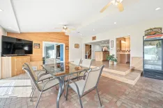 Spacious modern living room with dining area, brick flooring, and wood accents, including a kitchen bar and beverage fridge.