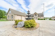 Elegant stone house with an attached two-car garage and a tiered water fountain in a landscaped front yard featuring a personalized stone signage.