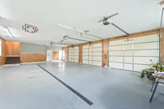 Spacious, clean two-car garage interior with epoxy flooring, wooden wall accents, utility sink, and storage, featuring two garage doors with openers and a side door leading outside.