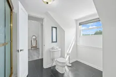 Bright, modern bathroom with a toilet, mirror, and window showing a blue sky.