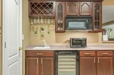 Kitchen interior with wooden cabinets, microwave, dishwasher, and a wine rack.