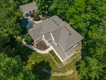 Aerial view of a large suburban home with a gray roof surrounded by green trees.