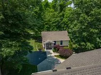 Aerial view of a single-family home with a shingled roof surrounded by green trees.