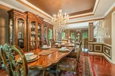 Elegant dining room with a long wooden table set for dinner, ornate cabinets, chandelier, and luxurious decor.