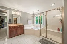 Spacious modern bathroom with a separate shower, jacuzzi tub, dual-sink vanity, tiled floor, and greenery outside the window.