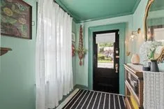Interior view of a room with light green walls, black and white striped floor, sheer white curtains, a front door partially open, and decorative elements like a mirror and wall art.
