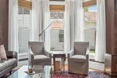 Bright living room interior with two armchairs, a sofa, sheer curtains, and a view of a balcony.
