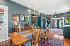 Elegant dining room with teal walls, hardwood floors, a wooden table set for six, and a chandelier, with a view into adjacent rooms.