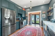 Interior of a modern kitchen with blue cabinets, stainless steel appliances, an oriental rug, and an open door leading to the outside.