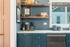 Modern kitchen interior with blue cabinets, floating shelves, and coffee maker.