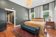 Elegantly furnished bedroom with a dark gray accent wall, large bed with gold bedding, navy blue sofa, oriental rug, and hardwood floors.