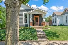 Charming single-story home with a covered front porch, manicured lawn, and a tree-lined sidewalk on a sunny day.