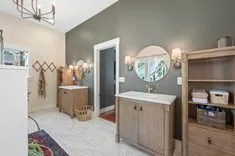 Contemporary bathroom interior with olive green walls, a wooden vanity with a circular mirror, and decorated with woven baskets and plants.