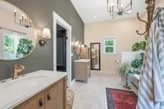 Elegant bathroom interior with a beige vanity, large mirror, decorative light fixtures, and a glimpse into the adjoining room.
