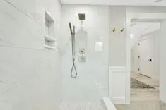 Modern bathroom interior with glass door walk-in shower, marble tiles, built-in wall shelf, and rainfall shower head.