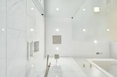 Modern bathroom with white marble tiles, glass shower enclosure, and gold fixtures.