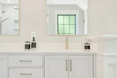 Elegant bathroom vanity with marble countertop, white cabinetry, and a large framed mirror reflecting a window.