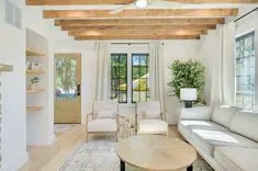 Bright and airy living room with wooden beams, large windows, comfortable seating, and a decorative indoor plant.