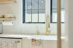 Bright modern kitchen with gold faucet, white farmhouse sink, and a window providing natural light.