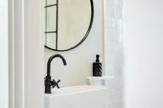 A modern bathroom sink with a matte black faucet, white subway tiles, and a round mirror with a black frame.