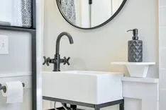 Modern bathroom interior with a white rectangular vessel sink, matte black faucet, towel, round mirror, and soap dispenser.