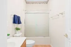 A clean, bright bathroom with a shower glass door, a toilet, a sink countertop, and a blue towel hanging on the wall.