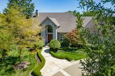 Two-story suburban house with a landscaped front yard and a stone pathway leading to an arched front entrance on a sunny day.