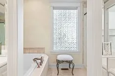 Elegant bathroom interior with a white bathtub, frosted glass window providing natural light, and a small cushioned stool.