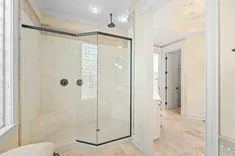 Elegant bathroom interior featuring a glass-enclosed shower with marble walls, seen through an open door with a view of a bedroom entrance in the background.