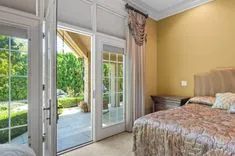 Bright bedroom with an open French door leading to a garden patio, elegant drapery, and a floral-patterned bedspread.