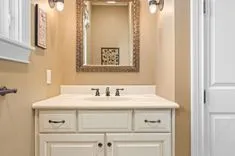 Elegant bathroom vanity with white cabinets, a cream countertop, and an ornate mirror framed by wall sconces and decorative artwork.