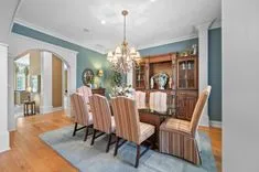 Elegant dining room with a wooden table, striped upholstered chairs, a chandelier, and a wooden china cabinet, with archways leading to adjacent rooms.