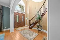 Elegant house entrance with wooden double doors, ornate stairway, and decorative rugs.