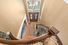 Elegant home entryway seen from the top of a staircase with hardwood floors, a large chandelier, and a double front door with glass panels.