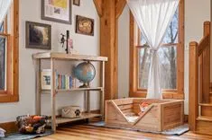 Cozy reading nook with a rustic wooden bookshelf, globe, and a pet bed next to a window with sheer curtains, in a room with wooden beams and walls.