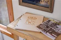 Open guestbook with "Cabin Guest Book" on cover and a photograph next to it on a wooden table, suggesting a cozy cabin setting.