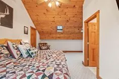 Cozy cabin bedroom interior with quilt-covered bed, wooden ceiling, wall art, and open wooden door.